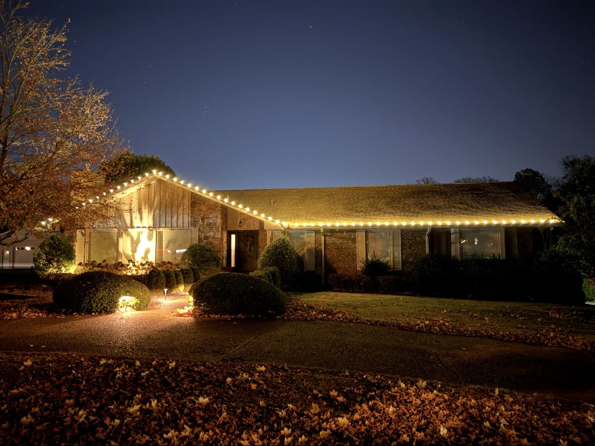Brick ranch home with warm white C9 roofline lighting under a dramatic starry dusk sky