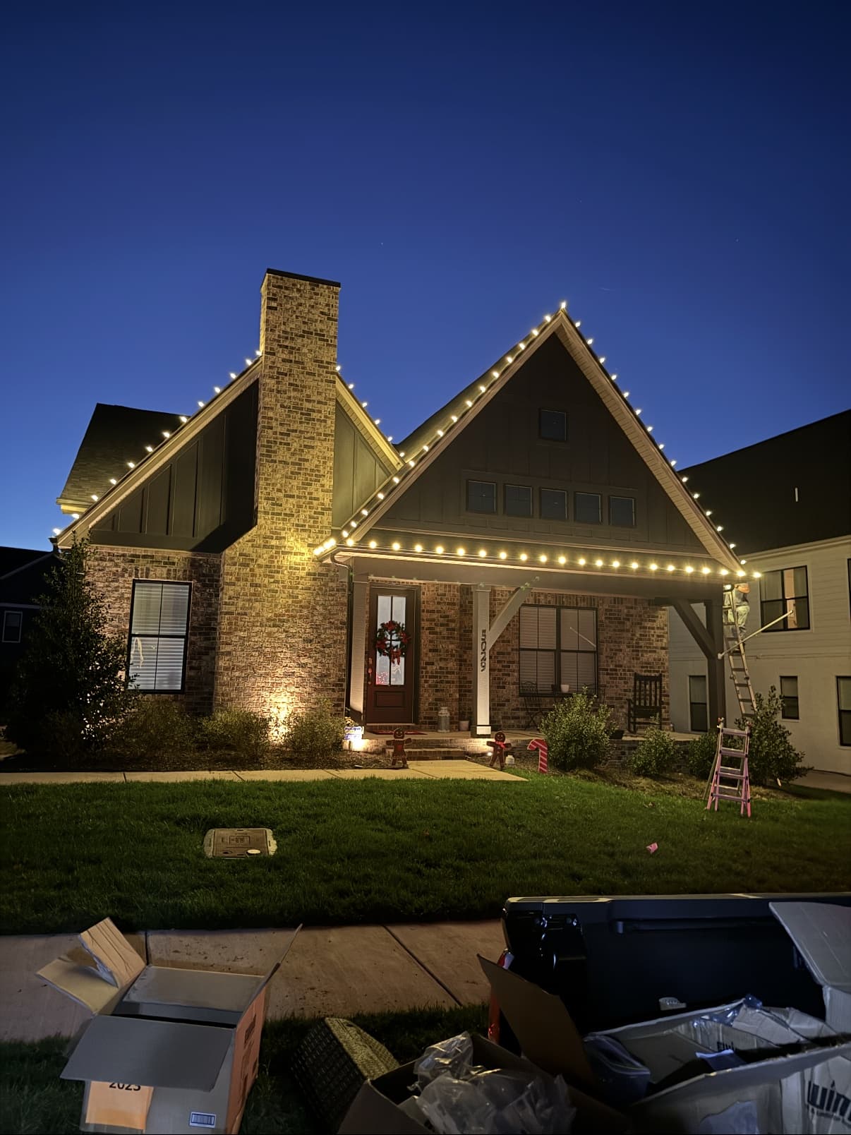 Installer on a ladder finishing a roofline C9 light installation at dusk